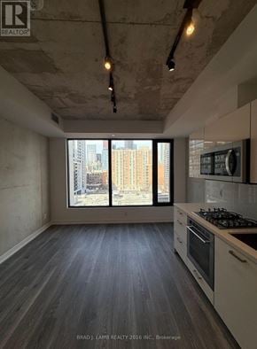 Toronto (Moss Park) condo for rent - A kitchen with a stove top oven and a window overlooking a city.