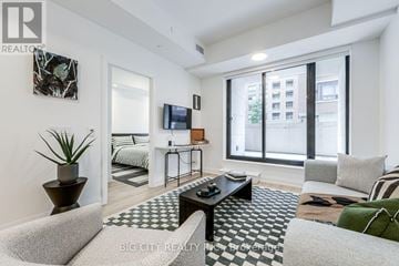 Toronto (Thorncliffe Park) condo for rent - A living room with a black and white checkered rug, a grey sofa, a black coffee table, a flat screen TV, and a large window with a view of a building.