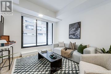 Toronto (Thorncliffe Park) condo for rent - A living room with a black and white checkered rug, a grey sofa, a coffee table, and a painting on the wall.