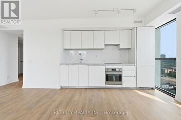 Toronto (Thorncliffe Park) condo for rent - A white kitchen with wooden floors and a large window.