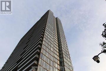 Toronto (South Parkdale) condo for rent - A tall building with a glass facade stands under a cloudy sky.