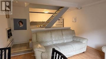 Toronto (Moss Park) townhouse for rent - A living room with a white couch and a staircase in the background.