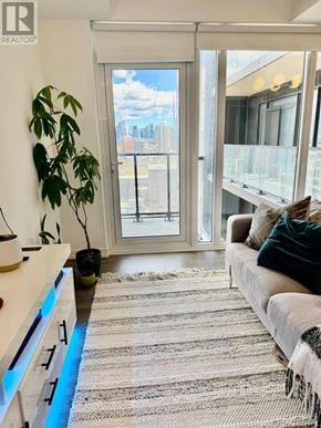 Toronto (South Parkdale) condo for rent - A living room with a couch, a plant, and a view of the city through a large window.