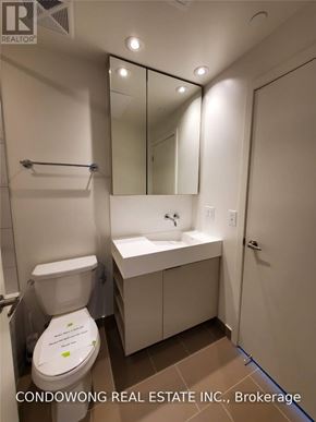 Toronto (Waterfront Communities) condo for rent - A white toilet with a sign on it is in a bathroom with a sink and mirror.