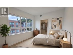 North Vancouver apartment for rent - A bedroom with a large bed, a potted plant, and a view of a building outside the window.