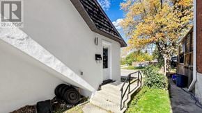 Kawartha Lakes (Lindsay) multi-family for rent - A white house with a black roof and a tree with yellow leaves in front of it.