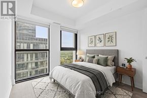 Toronto (Leaside) condo for rent - A bedroom with a large bed, a nightstand, and a window overlooking a cityscape.