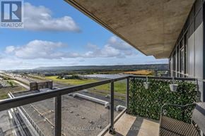 Grimsby (Grimsby Beach) condo for rent - A balcony with a metal railing and a green plant on the wall overlooks a parking lot and a highway.