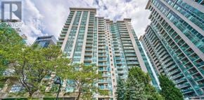 Toronto (Willowdale East) condo for rent - A tall building with many windows is surrounded by trees.