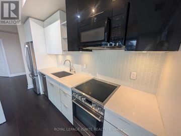 Toronto (Mimico) condo for rent - A kitchen with white cabinets and black appliances.