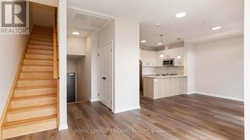 London North (North B) townhouse for rent - A room with a staircase and a kitchen area is on the market with Royal LePage Triland Realty.