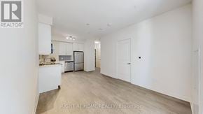 Toronto (Mimico) condo for rent - A spacious, empty room with a kitchen area to the left and a door to the right.