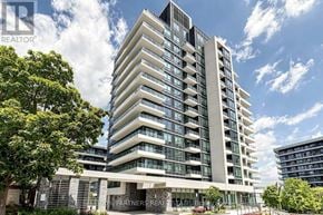 Toronto (Willowdale East) condo for rent - A tall, modern building with many windows and balconies, surrounded by greenery and a clear blue sky.