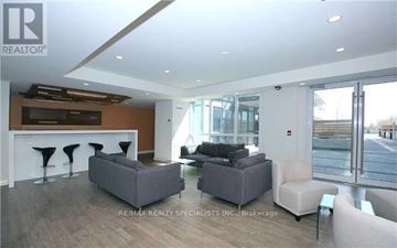 Toronto (Downsview-Roding-Cfb) condo for rent - A living room with a grey couch, a white armchair, and a bar area with stools.