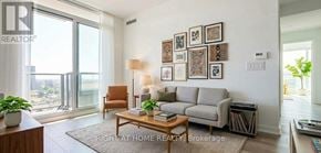 Toronto (Moss Park) condo for rent - A living room with a grey couch, a brown armchair, a coffee table, and a large window with a view of the city.