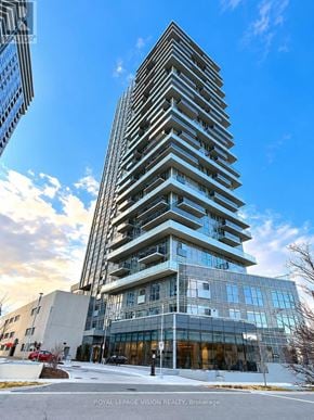 Toronto (Agincourt South-Malvern West) condo for rent - A tall, modern building with a glass facade stands in the foreground with a clear blue sky above.
