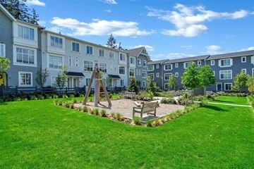 Surrey townhouse for rent - A playground area with a swing set and a wooden bench is located in the front yard of a residential building.