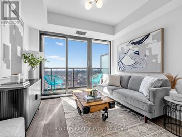Toronto (Leaside) condo for rent - A living room with a grey couch and a large window overlooking a cityscape.