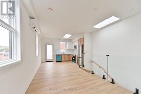 Toronto (Dovercourt-Wallace Emerson-Junction) townhouse for rent - A spacious room with wooden floors and white walls, featuring a kitchen area with a refrigerator, sink, and cabinets.