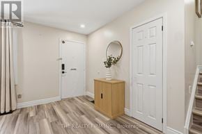 London East (East C) apartment for rent - A hallway with a wooden floor, a white door, a round mirror, and a wooden cabinet with a plant on top.