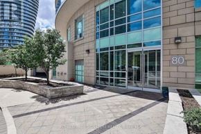 Mississauga (City Centre) condo for rent - A modern building with glass windows and a tree in a planter box in front of it.
