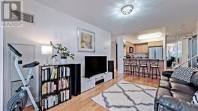 Toronto (Waterfront Communities) condo for rent - A living room with a black and white rug, a black leather couch, a white fireplace, and a bookshelf filled with books.