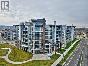 Stoney Creek condo for rent - A modern apartment building with a glass facade and a parking lot in front.