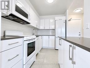 Toronto (University) condo for rent - A white kitchen with a black stove top oven and a microwave above it.
