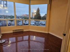 Mississauga (Cooksville) condo for rent - A room with wooden flooring and a large window overlooking a parking lot.