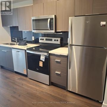 Toronto (Glenfield-Jane Heights) condo for rent - A stainless steel refrigerator stands in a kitchen with wooden cabinets and a microwave above the stove.