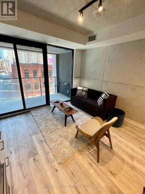 Toronto (Moss Park) condo for rent - A living room with a black couch, wooden coffee table, and a large window.