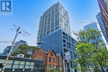 Toronto (Moss Park) condo for rent - A tall building with the number 30 on it stands in front of a crane and other buildings.