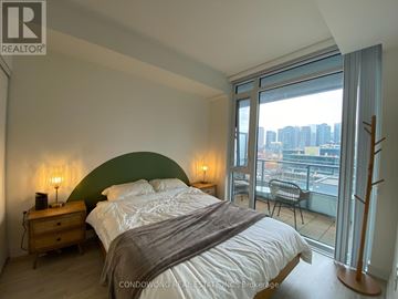 Toronto (Waterfront Communities) condo for rent - A bedroom with a large bed and a balcony overlooking a cityscape.
