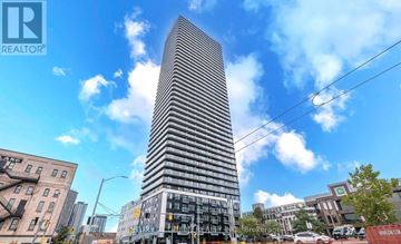 Kitchener condo for rent - A tall, modern building stands in the middle of a city street.
