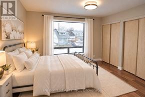 Windsor apartment for rent - A bedroom with a large bed, a nightstand with a lamp, and a window with a view of the neighborhood.