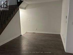Oshawa (Donevan) townhouse for rent - A room with wooden flooring and white walls, with a staircase on the left side.