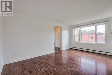 Whitby (Downtown Whitby) multi-family for rent - A room with wooden flooring and white walls, with a window showing a red building outside.
