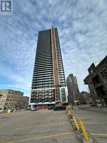 Kitchener condo for rent - A tall building with a glass facade stands in the middle of a parking lot.