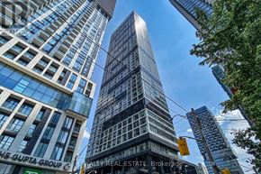 Toronto (Moss Park) condo for rent - A tall building with a glass facade stands in the middle of a cityscape.