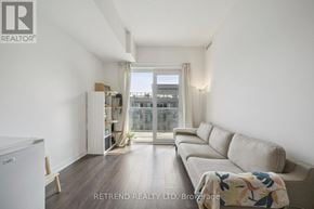Toronto (South Riverdale) condo for rent - A living room with a couch, a chair, and a window overlooking a cityscape.