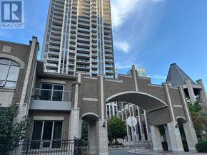 Mississauga (City Centre) condo for rent - A tall building with a modern glass facade stands behind a low brick building with a large arched entrance.