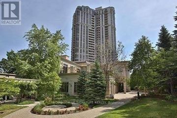 Toronto (Willowdale East) condo for rent - A large building with a tall tower is surrounded by trees and a well-maintained lawn.