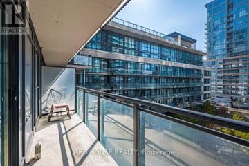 Toronto (Waterfront Communities) condo for rent - A balcony with a glass railing and a red chair overlooks a cityscape.