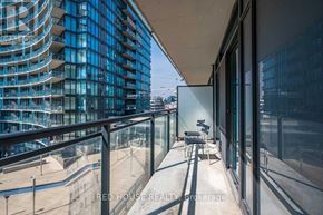 Toronto (Waterfront Communities) condo for rent - A balcony with a glass railing and a chair overlooking a cityscape.