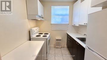 Toronto (Stonegate-Queensway) multi-family for rent - A small kitchen with a stove top oven and a refrigerator.
