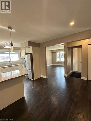 Kitchener apartment for rent - A well-lit, empty living space with wood flooring and a kitchen area to the left.