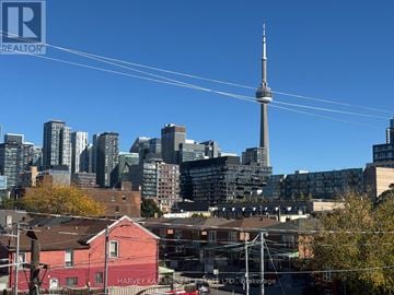 Toronto (Trinity-Bellwoods) multi-family for rent - A cityscape with a tall tower in the background and a red building in the foreground.