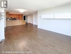 Burnaby apartment for rent - A spacious room with wooden flooring and a kitchen area in the background.
