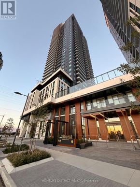 Vaughan (Vaughan Corporate Centre) condo for rent - A tall building with a glass facade stands next to a smaller building with a red and white facade.