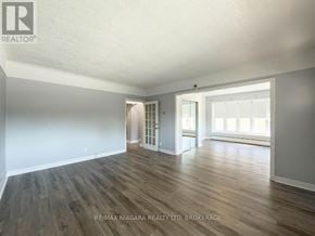 Niagara Falls (Clifton Hill) apartment for rent - A spacious room with wooden flooring and white walls, with a doorway leading to another room.